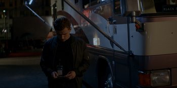 Movie still from “Ray Donovan: The Movie” (2022), directed by David Hollander – A man standing in front of a bus looking at his cell phone; Medium shot, Low angle