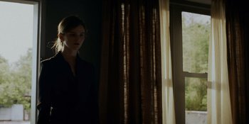Movie still from “Ray Donovan: The Movie” (2022), directed by David Hollander – A woman standing in front of a window in a dark room; Medium shot, Low angle