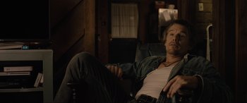 Movie still from “Raymond & Ray” (2022), directed by Rodrigo García – A man laying on a couch in a living room; Medium shot, Over the shoulder angle