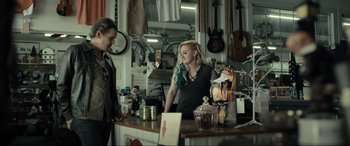 Movie still from “Raymond & Ray” (2022), directed by Rodrigo García – A woman standing at a counter in a music store; Medium shot, Over the shoulder angle