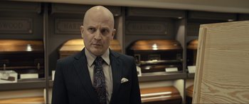 Movie still from “Raymond & Ray” (2022), directed by Rodrigo García – A man in a suit and tie standing in front of a casket; Close Up shot, Over the shoulder angle