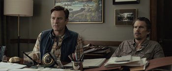 Movie still from “Raymond & Ray” (2022), directed by Rodrigo García – A man sitting at a table in front of a painting; Medium shot, Over the shoulder angle