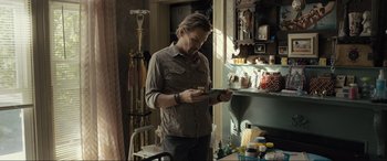 Movie still from “Raymond & Ray” (2022), directed by Rodrigo García – A man standing in front of a table holding a cell phone; Medium shot, Low angle