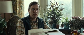 Movie still from “Raymond & Ray” (2022), directed by Rodrigo García – A man sitting at a table in front of potted plants; Close Up shot, Low angle