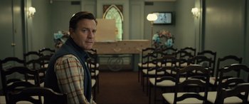 Movie still from “Raymond & Ray” (2022), directed by Rodrigo García – A man standing in front of chairs in a room; Medium shot, Over the shoulder angle