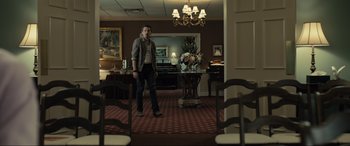 Movie still from “Raymond & Ray” (2022), directed by Rodrigo García – A man standing in a room with a vase of flowers on the floor; Wide shot, Low angle