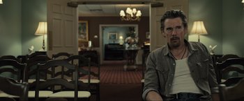 Movie still from “Raymond & Ray” (2022), directed by Rodrigo García – A man sitting at a table in front of a piano; Medium shot, Over the shoulder angle