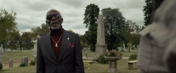 Movie still from “Raymond & Ray” (2022), directed by Rodrigo García – An older man wearing a suit and sunglasses in a cemetery; Medium shot, Low angle