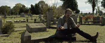 Movie still from “Raymond & Ray” (2022), directed by Rodrigo García – A man sitting on the ground in a cemetery; Medium shot, High angle