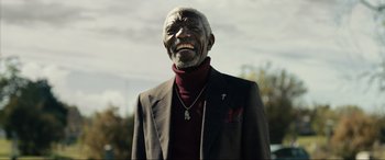 Movie still from “Raymond & Ray” (2022), directed by Rodrigo García – An older man wearing a suit and a cross necklace; Medium shot, Low angle