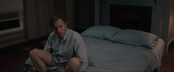 Movie still from “Raymond & Ray” (2022), directed by Rodrigo García – A man sitting on a bed in front of a pillow; Medium shot, High angle