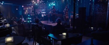 Movie still from “Raymond & Ray” (2022), directed by Rodrigo García – A group of people sitting at tables in front of a microphone; Extreme Wide shot, High angle