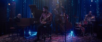 Movie still from “Raymond & Ray” (2022), directed by Rodrigo García – A man sitting in front of a microphone while a man plays a double bass; Wide shot, Low angle