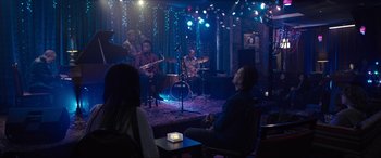 Movie still from “Raymond & Ray” (2022), directed by Rodrigo García – A group of people sitting on a stage playing music; Extreme Wide shot, Over the shoulder angle