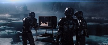 Movie still from “Ready Player One” (2018), directed by Steven Spielberg – A group of people standing around a television; Wide shot, Over the shoulder angle