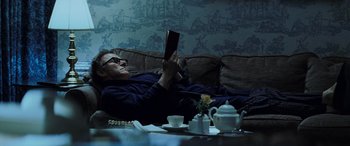 Movie still from “Red Dragon” (2002), directed by Brett Ratner – A man laying on a couch reading a book; Medium shot, High angle