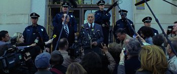 Movie still from “Red Dragon” (2002), directed by Brett Ratner – A man in a suit and tie standing in front of microphones; Medium shot, Over the shoulder angle