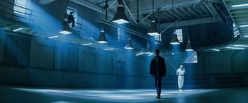 A man is walking in a room with lights hanging from the ceiling
