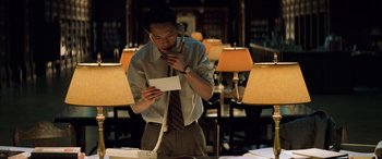 Movie still from “Red Dragon” (2002), directed by Brett Ratner – A man standing at a table holding a phone to his ear and looking at a piece of paper; Medium shot, Low angle