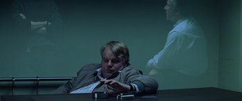 Movie still from “Red Dragon” (2002), directed by Brett Ratner – A man sitting at a table smoking a cigarette in front of a projector screen; Medium shot, Over the shoulder angle
