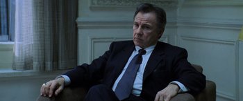 Movie still from “Red Dragon” (2002), directed by Brett Ratner – An older man wearing a suit and tie sitting in a chair; Close Up shot, Low angle