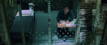 Movie still from “Red Dragon” (2002), directed by Brett Ratner – A man sitting at a table in a jail cell; Wide shot, Overhead angle