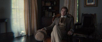 Movie still from “Redeeming Love” (2022), directed by D.J. Caruso – A man sitting in a chair wearing a suit and hat; Medium shot, High angle