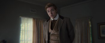 Movie still from “Redeeming Love” (2022), directed by D.J. Caruso – A man in a suit and tie standing next to a window; Medium shot, Over the shoulder angle
