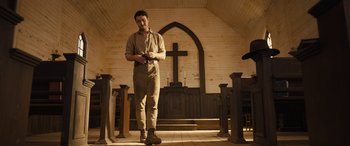 Movie still from “Redeeming Love” (2022), directed by D.J. Caruso – A man standing in front of a cross in a church; Wide shot, Low angle