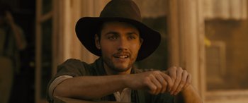 Movie still from “Redeeming Love” (2022), directed by D.J. Caruso – A man wearing a brown hat sitting in front of a window; Close Up shot, Over the shoulder angle