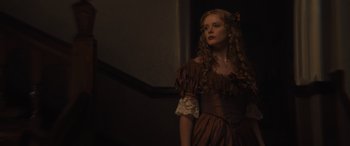 Movie still from “Redeeming Love” (2022), directed by D.J. Caruso – A woman in a brown dress standing next to a staircase; Close Up shot, Low angle