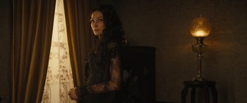 Movie still from “Redeeming Love” (2022), directed by D.J. Caruso – A woman in a black dress sitting in front of a window; Close Up shot, Over the shoulder angle