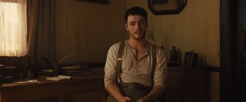 Movie still from “Redeeming Love” (2022), directed by D.J. Caruso – A man sitting on a chair in a room; Medium shot, Low angle