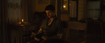 Movie still from “Redeeming Love” (2022), directed by D.J. Caruso – A man sitting in a chair reading a book; Medium shot, Low angle
