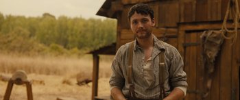 Movie still from “Redeeming Love” (2022), directed by D.J. Caruso – A man wearing suspenders standing in front of a wooden structure; Close Up shot, Over the shoulder angle