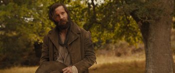 Movie still from “Redeeming Love” (2022), directed by D.J. Caruso – A man with long hair and a beard standing in a field; Medium shot, Over the shoulder angle