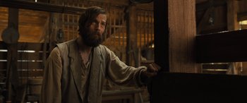 Movie still from “Redeeming Love” (2022), directed by D.J. Caruso – A bearded man in a brown shirt is leaning against a wall; Medium shot, Low angle