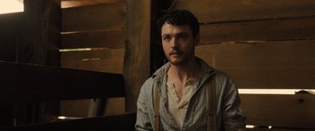 Movie still from “Redeeming Love” (2022), directed by D.J. Caruso – A man with a beard is standing in front of a wooden wall; Close Up shot, Low angle