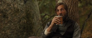 Movie still from “Redeeming Love” (2022), directed by D.J. Caruso – A man sitting in front of a tree drinking a beverage; Medium shot, Over the shoulder angle