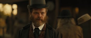 Movie still from “Redeeming Love” (2022), directed by D.J. Caruso – A man with a long beard wearing a top hat; Close Up shot, Over the shoulder angle