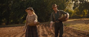 Movie still from “Redeeming Love” (2022), directed by D.J. Caruso – A man and a woman holding baskets on a dirt field; Medium shot, Low angle
