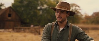 Movie still from “Redeeming Love” (2022), directed by D.J. Caruso – A man with a hat and a beard is standing in a field; Close Up shot, Over the shoulder angle