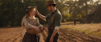 Movie still from “Redeeming Love” (2022), directed by D.J. Caruso – A man touching a woman's forehead while standing on a dirt road; Medium shot, Low angle