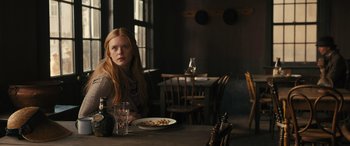 Movie still from “Redeeming Love” (2022), directed by D.J. Caruso – A woman sitting at a table with a plate of food in front of her; Medium shot, Over the shoulder angle