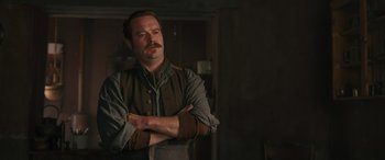 Movie still from “Redeeming Love” (2022), directed by D.J. Caruso – A man standing with his arms crossed in front of a wall; Medium shot, Low angle