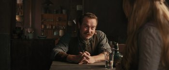 Movie still from “Redeeming Love” (2022), directed by D.J. Caruso – A man sitting at a table with a glass of water; Medium shot, Over the shoulder angle
