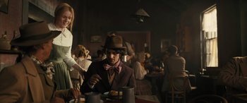 Movie still from “Redeeming Love” (2022), directed by D.J. Caruso – A man wearing a hat eating a plate of food at a restaurant; Medium shot, Low angle