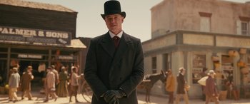Movie still from “Redeeming Love” (2022), directed by D.J. Caruso – A man in a top hat and gloves standing in front of a building; Medium shot, Low angle