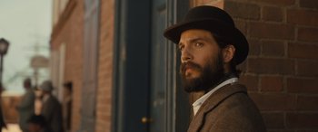 Movie still from “Redeeming Love” (2022), directed by D.J. Caruso – A man with a beard wearing a suit and a hat; Close Up shot, Low angle