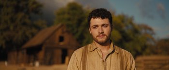 Movie still from “Redeeming Love” (2022), directed by D.J. Caruso – A man with a beard is standing in front of an old house; Close Up shot, Low angle